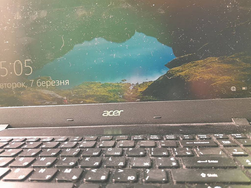 Екран ноутбука Acer відображає дату і час: "5:05, Вівторок, 7 березня". Видно частину клавіатури і панель дисплея, яка має трохи пилу. На екрані відображається пейзаж, який є стандартною заставкою Windows.