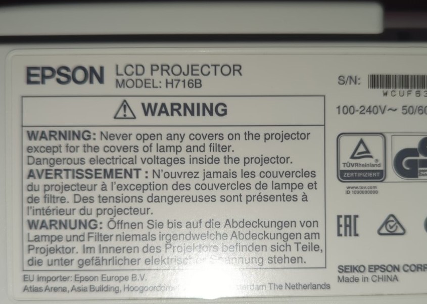 epson-projector-model-h716b-warning-label.jpg Зображення попереджувальної наклейки на проекторі Epson, модель H716B, з інструкціями щодо безпеки англійською, французькою та німецькою мовами.