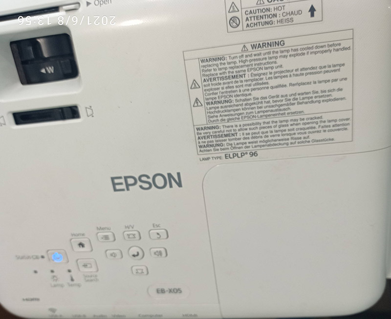 Верхня панель Epson EB-X05 з елементами управління та попередженнями Верхня панель проектора Epson EB-X05 з елементами управління, зокрема кнопками Home, Menu, H/V, а також інформаційними попередженнями про безпечну експлуатацію лампи типу ELPLP96.