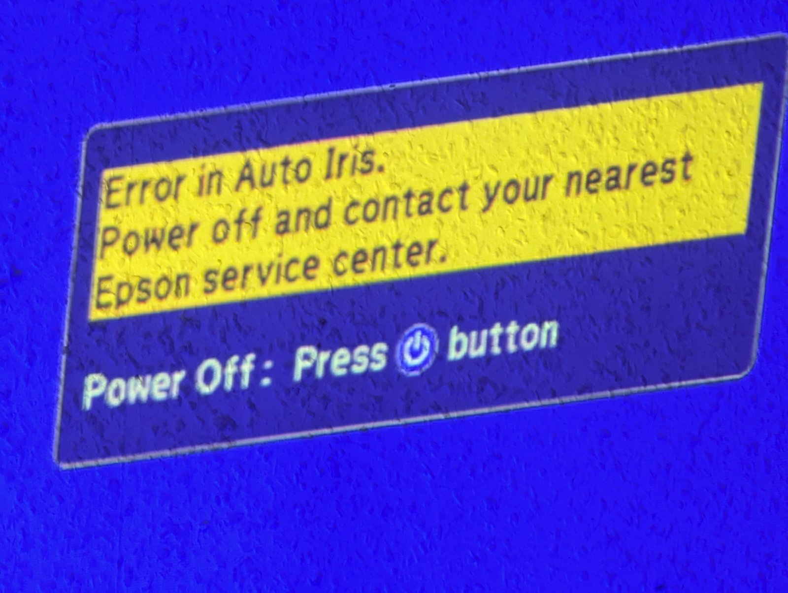 Помилка Auto Iris на проекторі Epson - зверніться до сервісу Проекція повідомлення на екрані, де зазначено помилку "Error in Auto Iris" на синьому фоні, що вимагає звернення до сервісного центру Epson для подальшої діагностики.