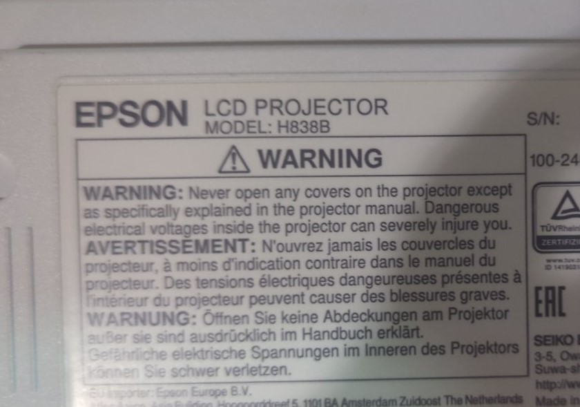 Наклейка з технічними характеристиками проектора Epson H838B Наклейка з попереджувальними написами та технічними характеристиками на проекторі Epson H838B. Вказано інформацію про електричні напруги та застереження щодо безпечного використання пристрою.