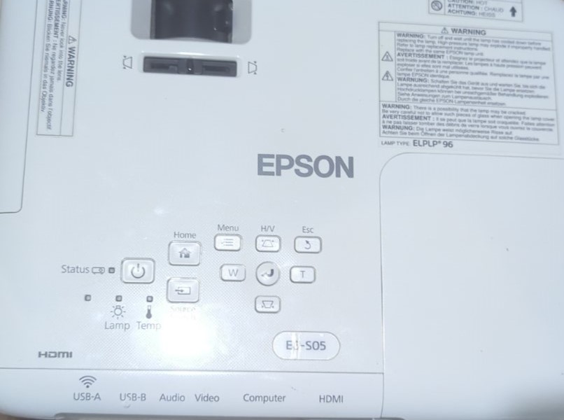 Панель управління проектора Epson EB-S05 Верхня частина проектора Epson EB-S05 з кнопками управління. Видно основні елементи, такі як кнопка живлення, статусні індикатори для лампи та температури, а також меню управління проєкцією. Ідеальний вибір для офісів та навчальних закладів.